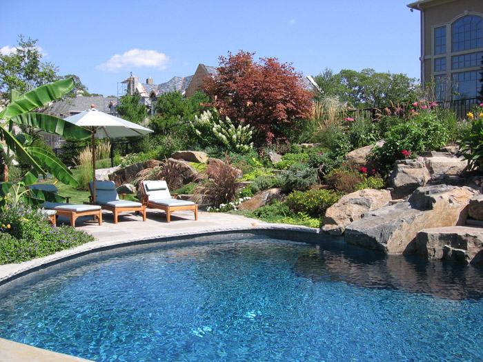 An artificial stone waterfall with lush landscaping in both urns and planted  around the waterfall